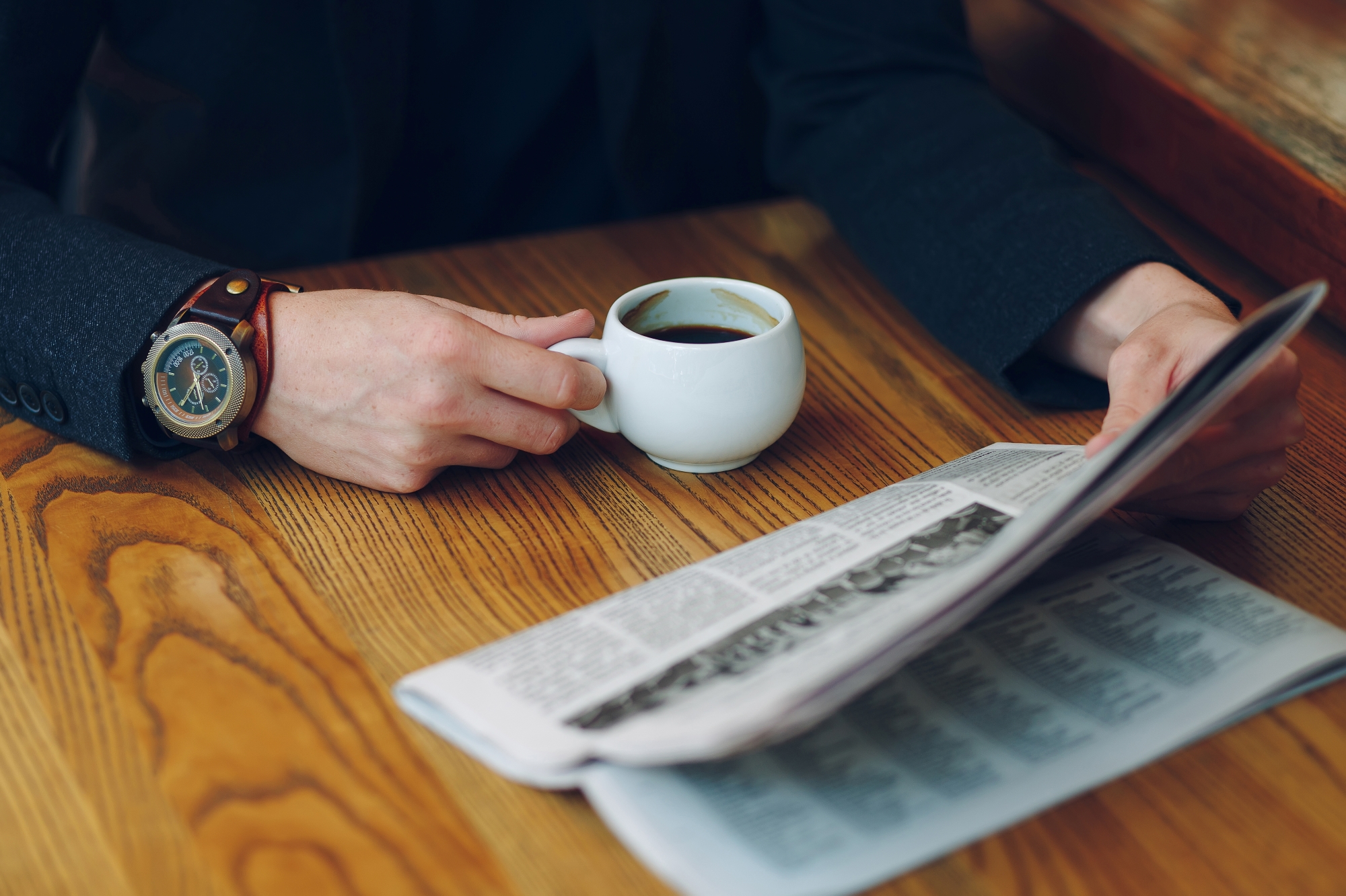 a person reading the newspaper and drinking coffee